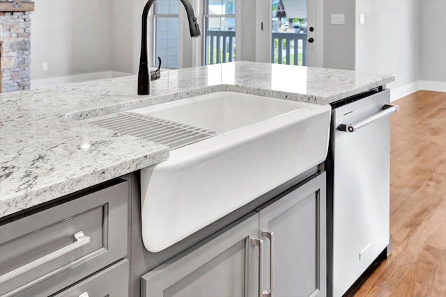 kitchen with stainless steel dishwasher, light hardwood / wood-style flooring, light stone counters, and sink