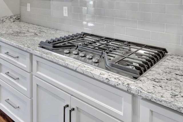 details featuring stainless steel gas stovetop, light stone counters, white cabinets, and decorative backsplash