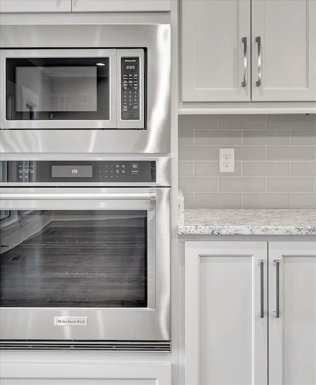 room details with light stone counters, backsplash, appliances with stainless steel finishes, and white cabinets