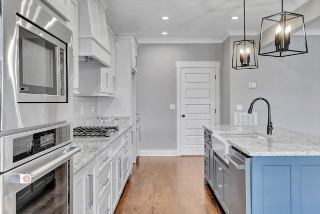 kitchen with wood-type flooring, premium range hood, a kitchen island with sink, stainless steel appliances, and white cabinets