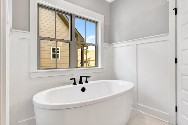 bathroom featuring a soaking tub, wainscoting, and a decorative wall