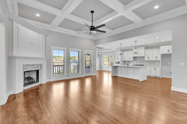 unfurnished living room featuring beam ceiling, coffered ceiling, light wood-type flooring, and a high end fireplace