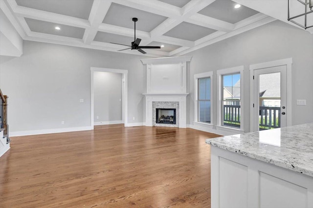 unfurnished living room featuring ceiling fan, coffered ceiling, beamed ceiling, and light hardwood / wood-style flooring