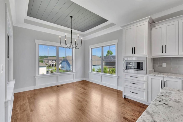 unfurnished dining area featuring an inviting chandelier, ornamental molding, dark wood-type flooring, and a raised ceiling