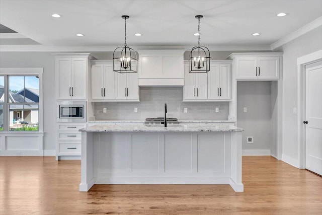 kitchen with white cabinetry, stainless steel microwave, decorative light fixtures, and light stone counters