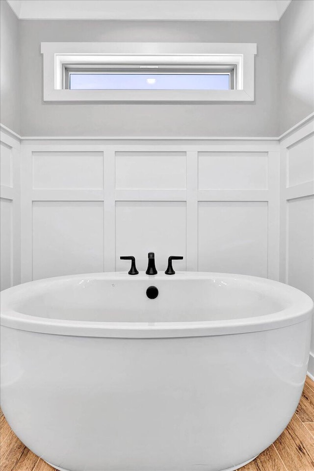 full bath featuring a soaking tub, a decorative wall, and wood finished floors