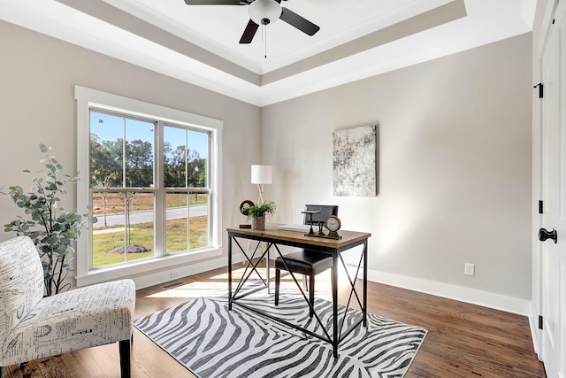 office with a ceiling fan, wood finished floors, baseboards, ornamental molding, and a raised ceiling