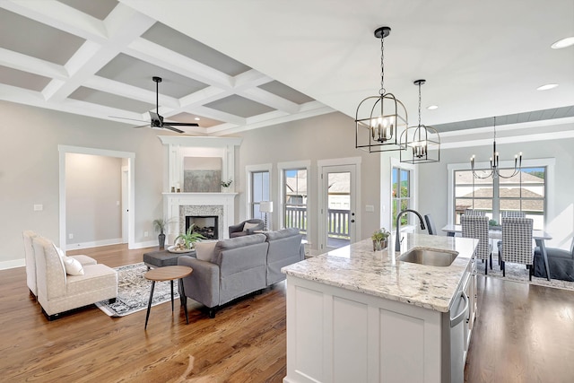 kitchen featuring an island with sink, beam ceiling, a fireplace, wood finished floors, and a sink