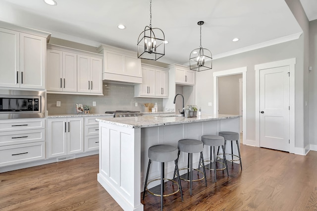 kitchen featuring a sink, stainless steel microwave, backsplash, wood finished floors, and white cabinets