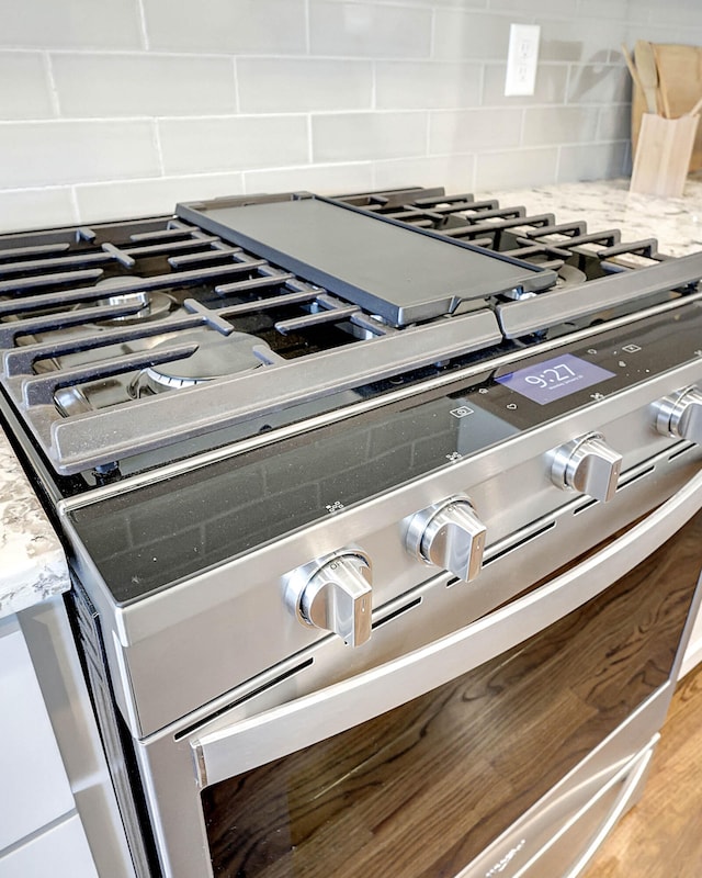 interior details with wood-type flooring, high end stove, light stone counters, and backsplash