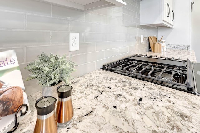 kitchen with white cabinetry, backsplash, black gas cooktop, and light stone counters