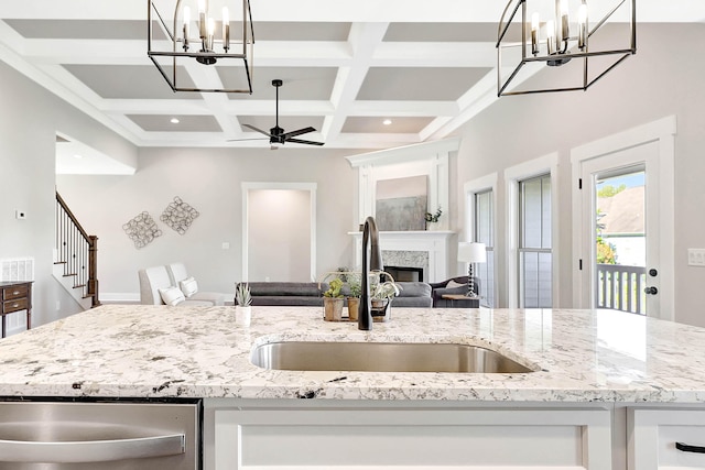 kitchen with ceiling fan with notable chandelier, a sink, a glass covered fireplace, open floor plan, and dishwasher