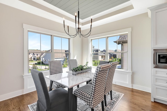 dining area featuring a tray ceiling, wood finished floors, crown molding, baseboards, and a chandelier