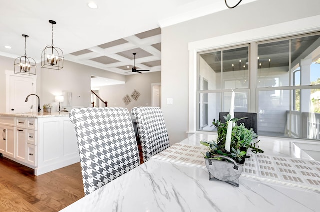 dining space featuring sink, ceiling fan with notable chandelier, coffered ceiling, beamed ceiling, and dark wood-type flooring