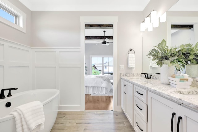 bathroom with beamed ceiling, wood finished floors, double vanity, a freestanding tub, and a decorative wall