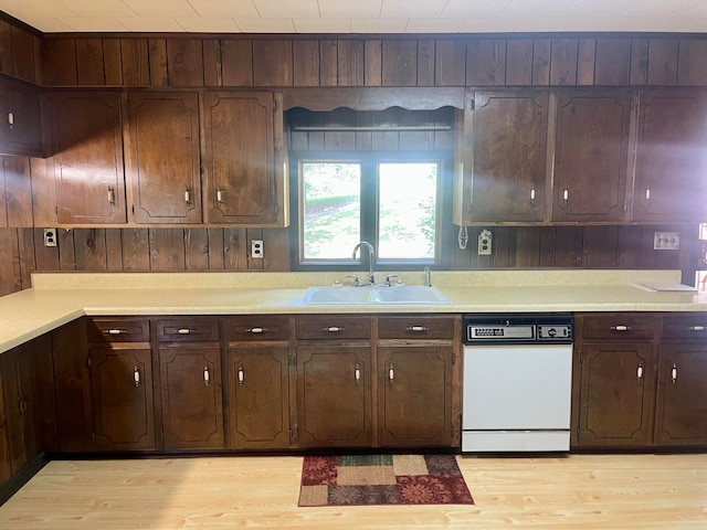 kitchen with white dishwasher, wooden walls, light hardwood / wood-style floors, and sink