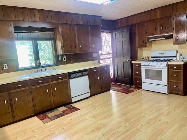 kitchen with light wood-type flooring, sink, white appliances, and wooden walls