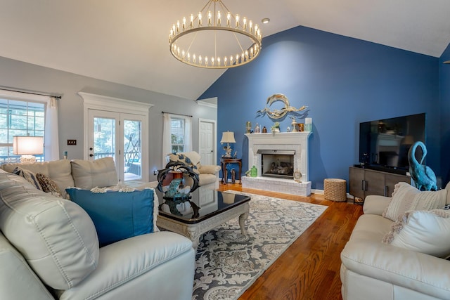 living room with a notable chandelier, lofted ceiling, dark wood-type flooring, and a brick fireplace