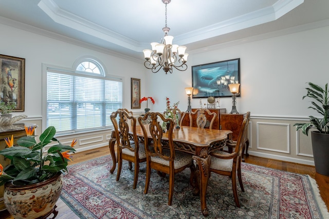 dining room with a chandelier, hardwood / wood-style flooring, a raised ceiling, and crown molding