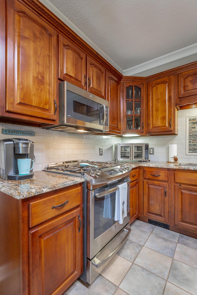 kitchen featuring light stone countertops, backsplash, ornamental molding, stainless steel appliances, and light tile patterned floors