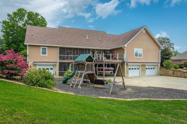 rear view of house with a playground, a garage, a lawn, and a sunroom