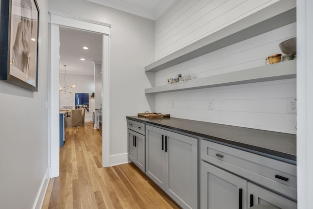 bar featuring ornamental molding, a chandelier, gray cabinetry, and light hardwood / wood-style floors