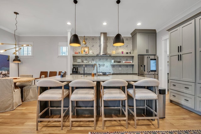 kitchen featuring light wood-type flooring, stainless steel fridge, a kitchen breakfast bar, decorative backsplash, and wall chimney exhaust hood