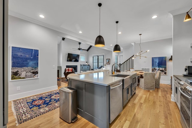 kitchen featuring a large fireplace, ceiling fan with notable chandelier, stainless steel appliances, light hardwood / wood-style floors, and an island with sink