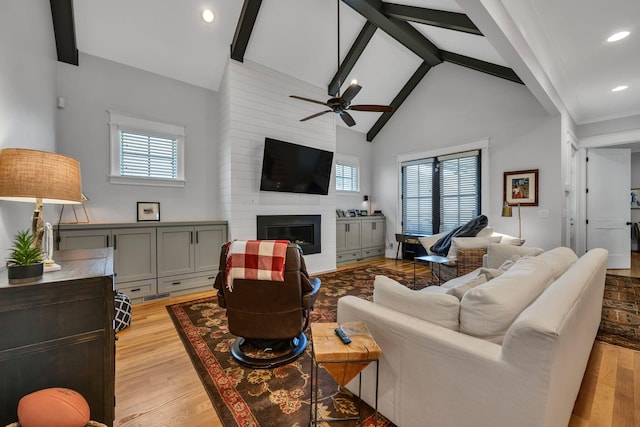 living room with light wood-type flooring, a large fireplace, high vaulted ceiling, ceiling fan, and beam ceiling