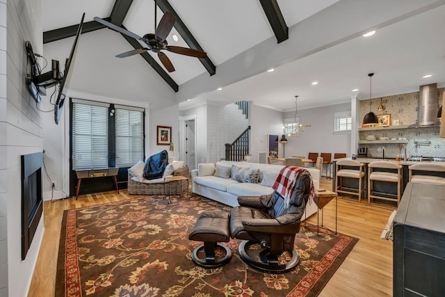 living room featuring ceiling fan with notable chandelier, light hardwood / wood-style flooring, and vaulted ceiling with beams