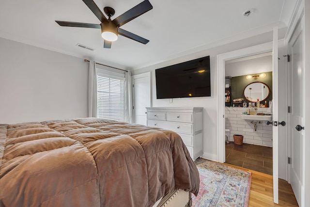 bedroom featuring ensuite bathroom, light wood-type flooring, sink, brick wall, and ceiling fan