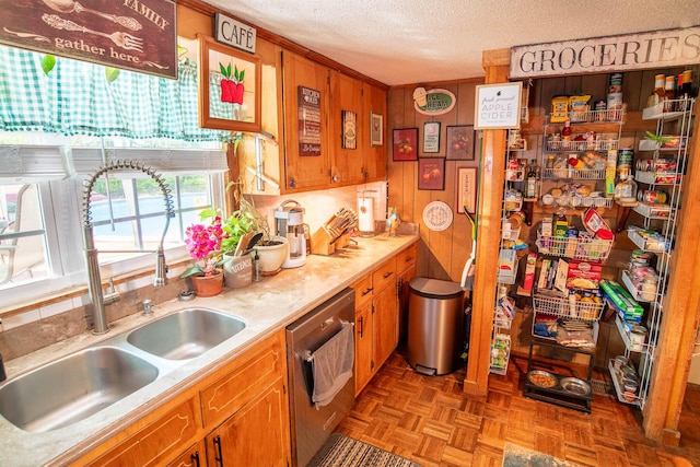 kitchen featuring brown cabinetry, a sink, light countertops, a textured ceiling, and stainless steel dishwasher