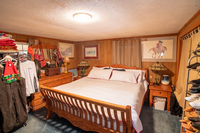 bedroom featuring a textured ceiling, wood walls, and dark colored carpet