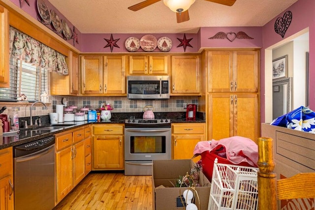 kitchen featuring a textured ceiling, stainless steel appliances, sink, ceiling fan, and light wood-type flooring