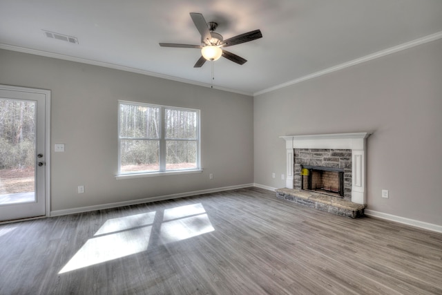 unfurnished living room featuring ceiling fan, ornamental molding, wood-type flooring, and a stone fireplace