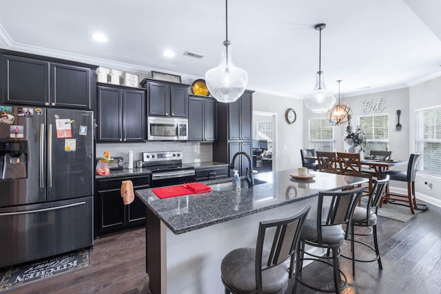 kitchen featuring a kitchen breakfast bar, dark hardwood / wood-style flooring, pendant lighting, appliances with stainless steel finishes, and a kitchen island with sink