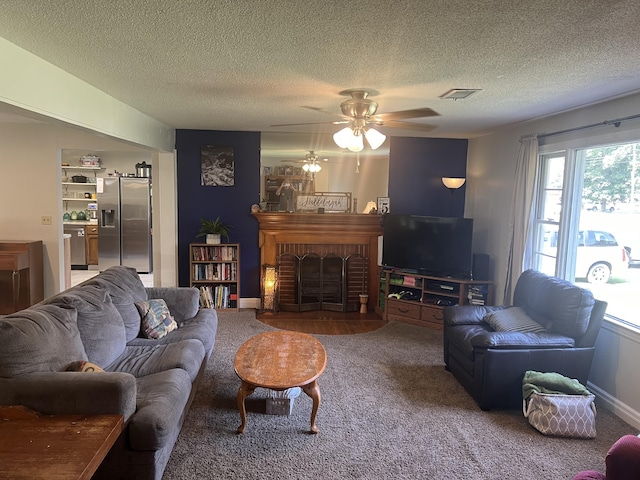 carpeted living room with a textured ceiling, ceiling fan, visible vents, and a brick fireplace