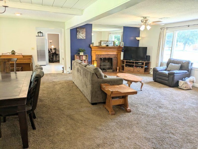 carpeted living room featuring a textured ceiling, ceiling fan, a brick fireplace, and beam ceiling