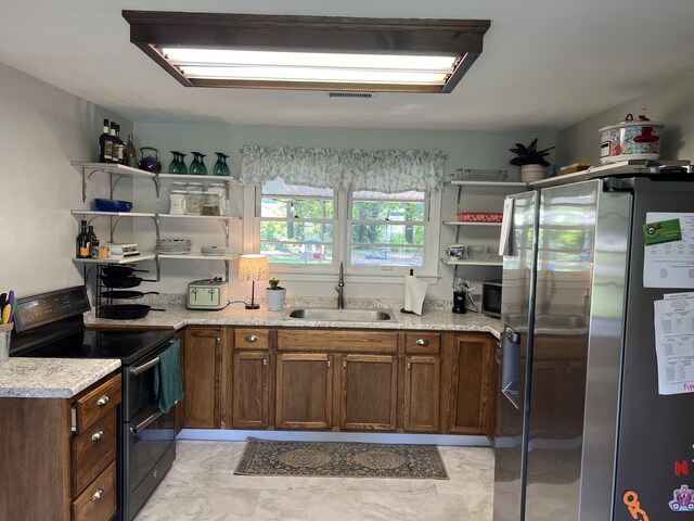 kitchen featuring light stone counters, electric range, stainless steel fridge, and sink