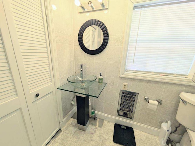 bathroom with heating unit, toilet, and tile walls