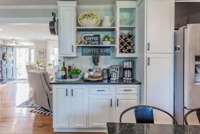 bar featuring stainless steel fridge with ice dispenser, dark stone counters, white cabinets, and light wood-type flooring