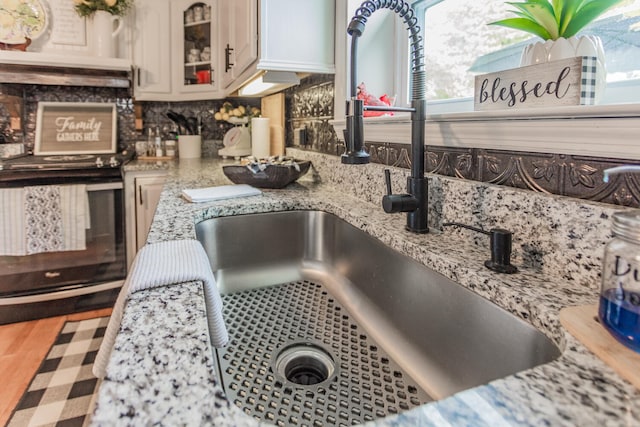 interior details with sink, light stone countertops, white cabinets, and stainless steel range with electric stovetop