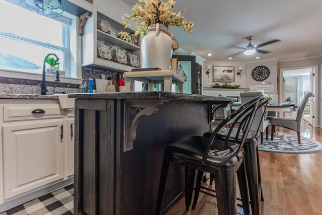 kitchen featuring light hardwood / wood-style flooring, a kitchen bar, crown molding, ceiling fan, and white cabinets