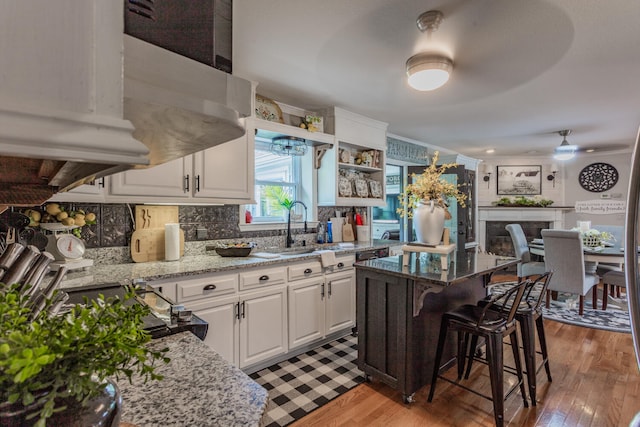 kitchen with white cabinets, light wood-type flooring, light stone countertops, ceiling fan, and a kitchen island