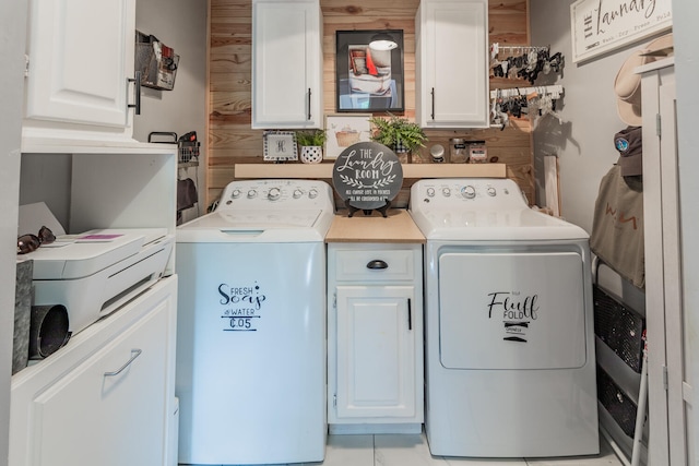 clothes washing area with cabinets, independent washer and dryer, and wood walls