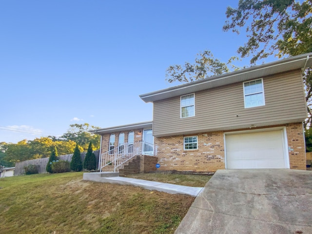 split level home featuring a front yard, fence, concrete driveway, a garage, and brick siding