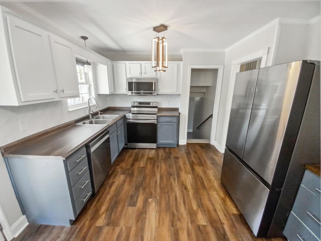 kitchen with dark countertops, ornamental molding, stainless steel appliances, white cabinetry, and a sink