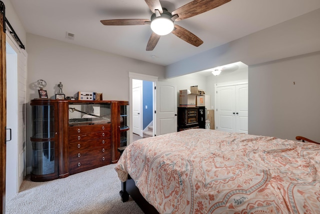 bedroom with light carpet, a closet, ceiling fan, and a barn door