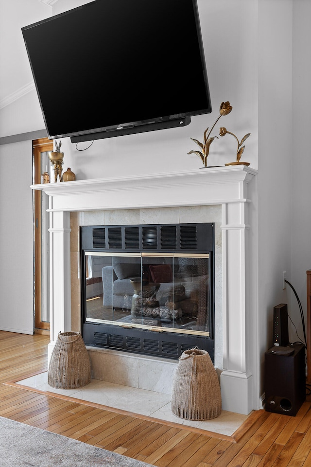 interior details featuring crown molding, wood-type flooring, and a tile fireplace