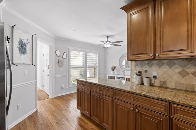 kitchen with crown molding, light stone countertops, light hardwood / wood-style floors, stainless steel fridge, and ceiling fan